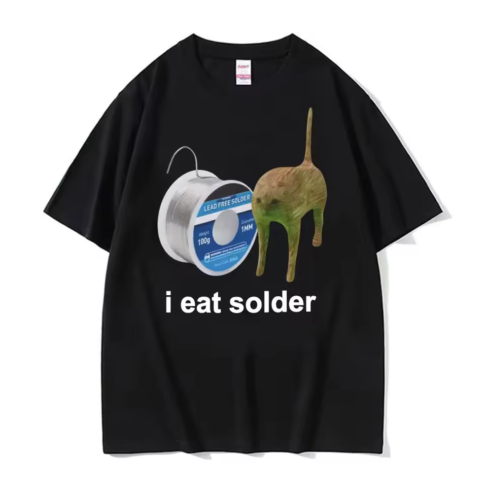a black t-shirt featuring a roll of solder next to an extremely stiff orange cat with a compressed neck and tail pointing directly upwards like an antenna. the bottom of the shirt reads "i eat solder"