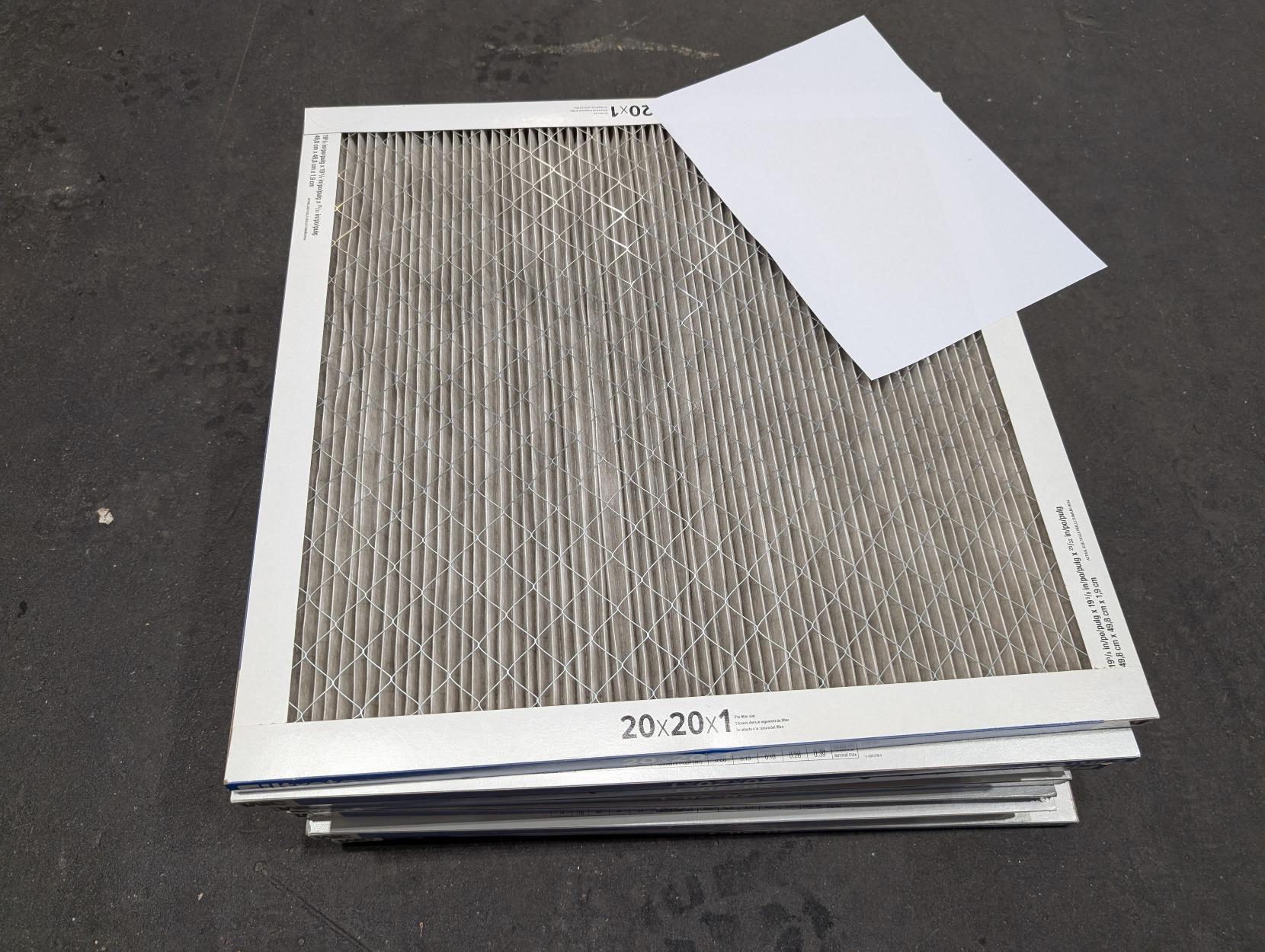 a stack of square air filters, with a white a4 page for reference. the filtering part of the filter looks pretty dark