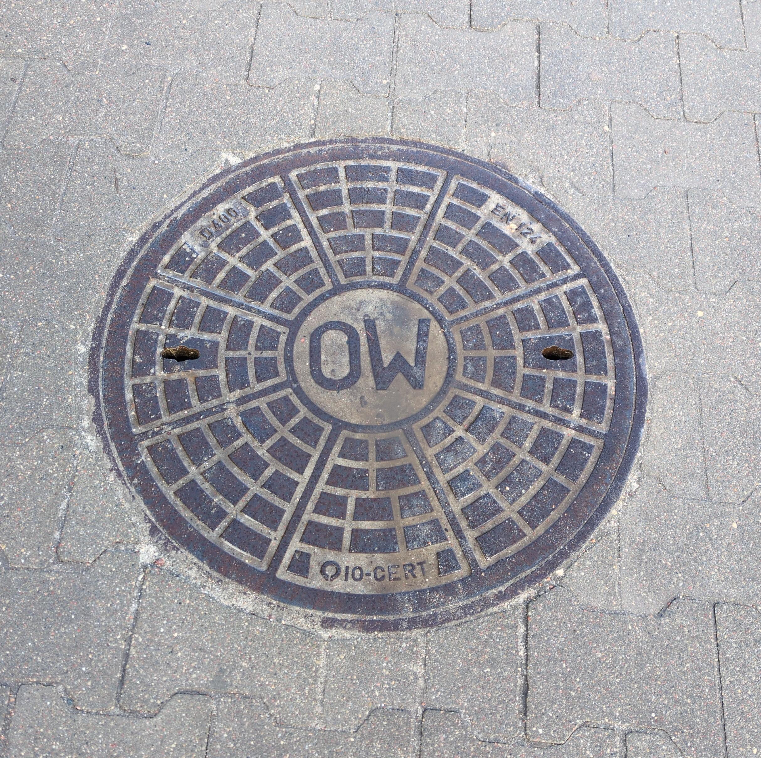 An iron manhole in the pavement, with the letters "OW" embossed in the middle.