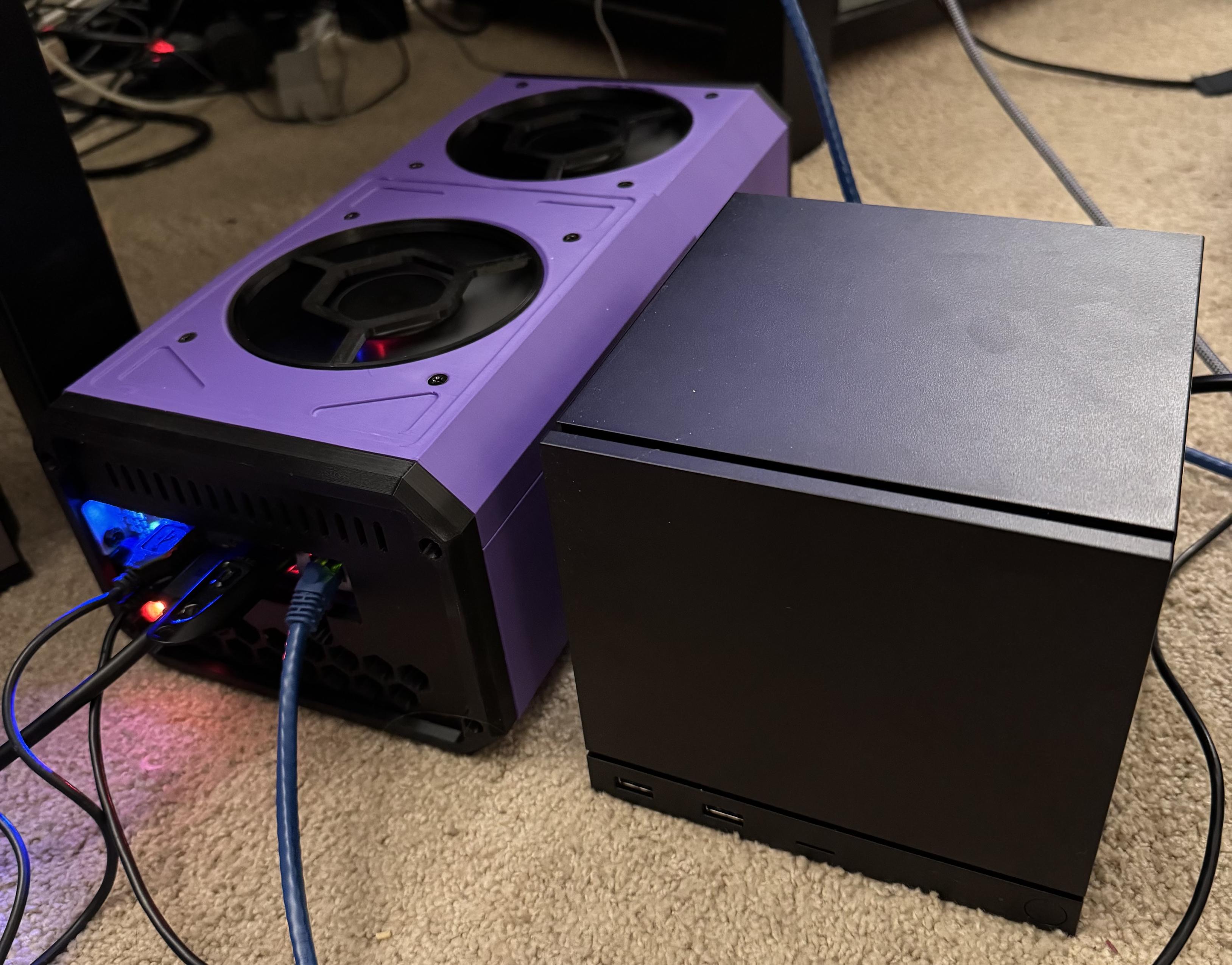 A photo of two electronics: one is a long case with a chamfered purple design with two big fans on the top and some cables coming out of the front (the BC-250). Next to it is an austere black cube design with a removable front panel and some USB ports on the bottom (the Steam Machine). The cube is slightly taller than the BC-250 but much less long and a bit wider.