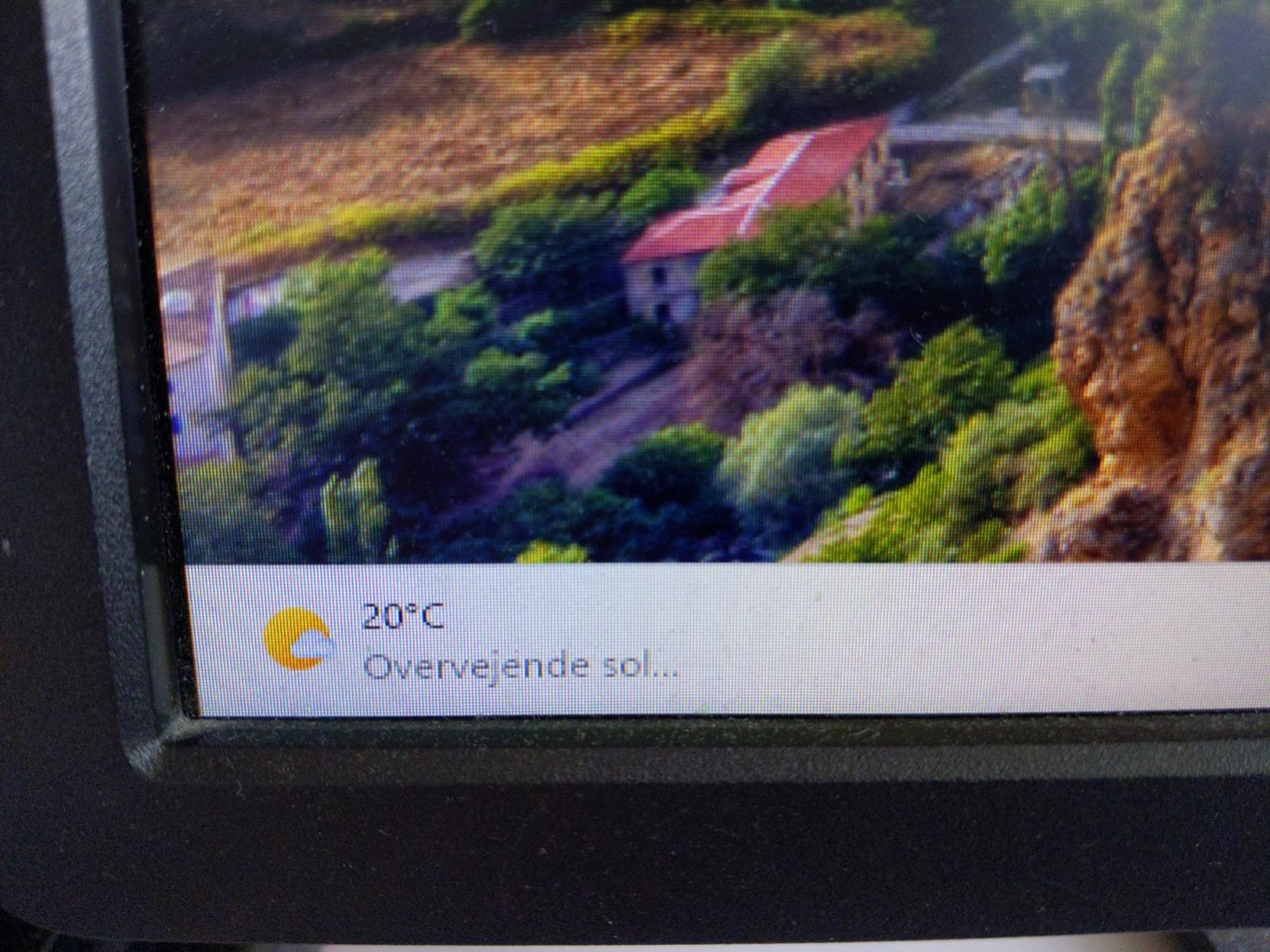 Photo of the corner of a computer display, where Windows 11 shows its built-in weather info widget. It says "20°C, Overvejende sol..."