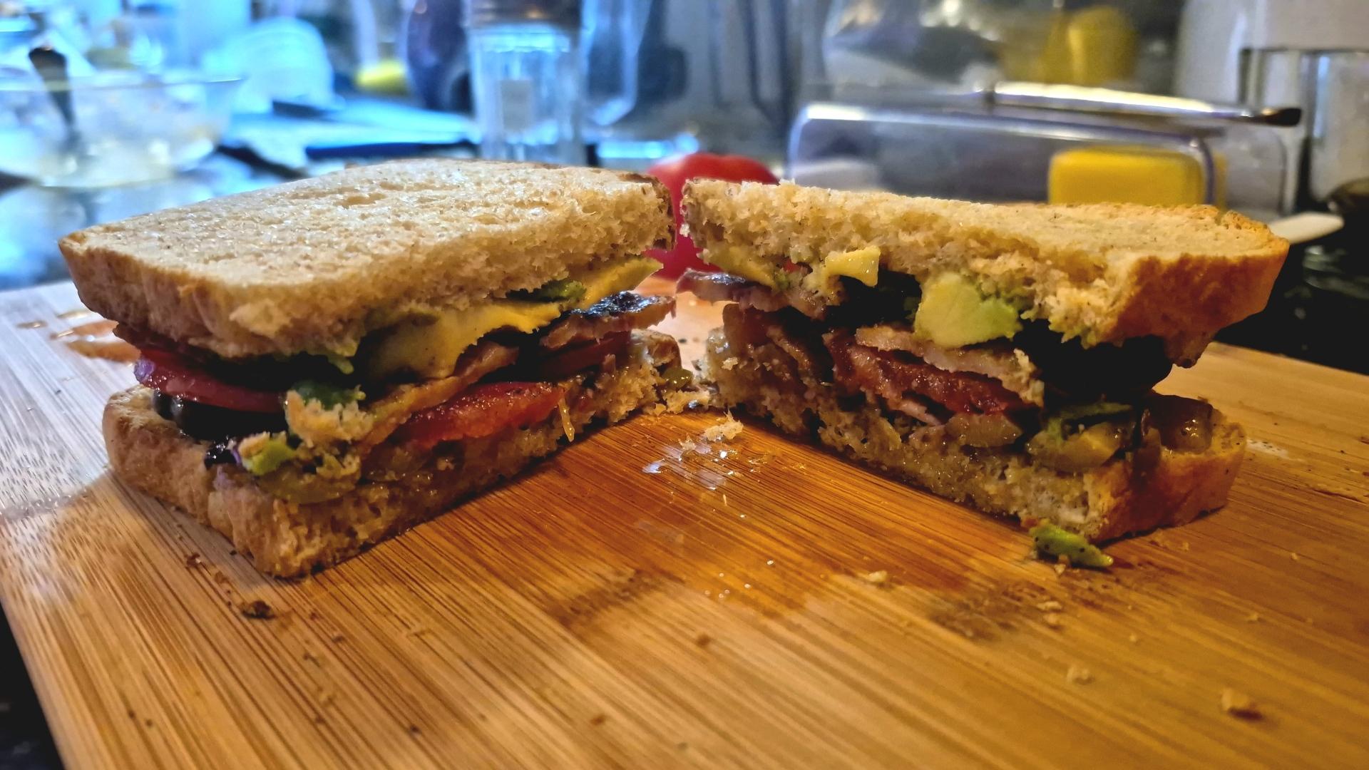 a sandwich filled with tomatoes, avocado, bacon, and olive salad