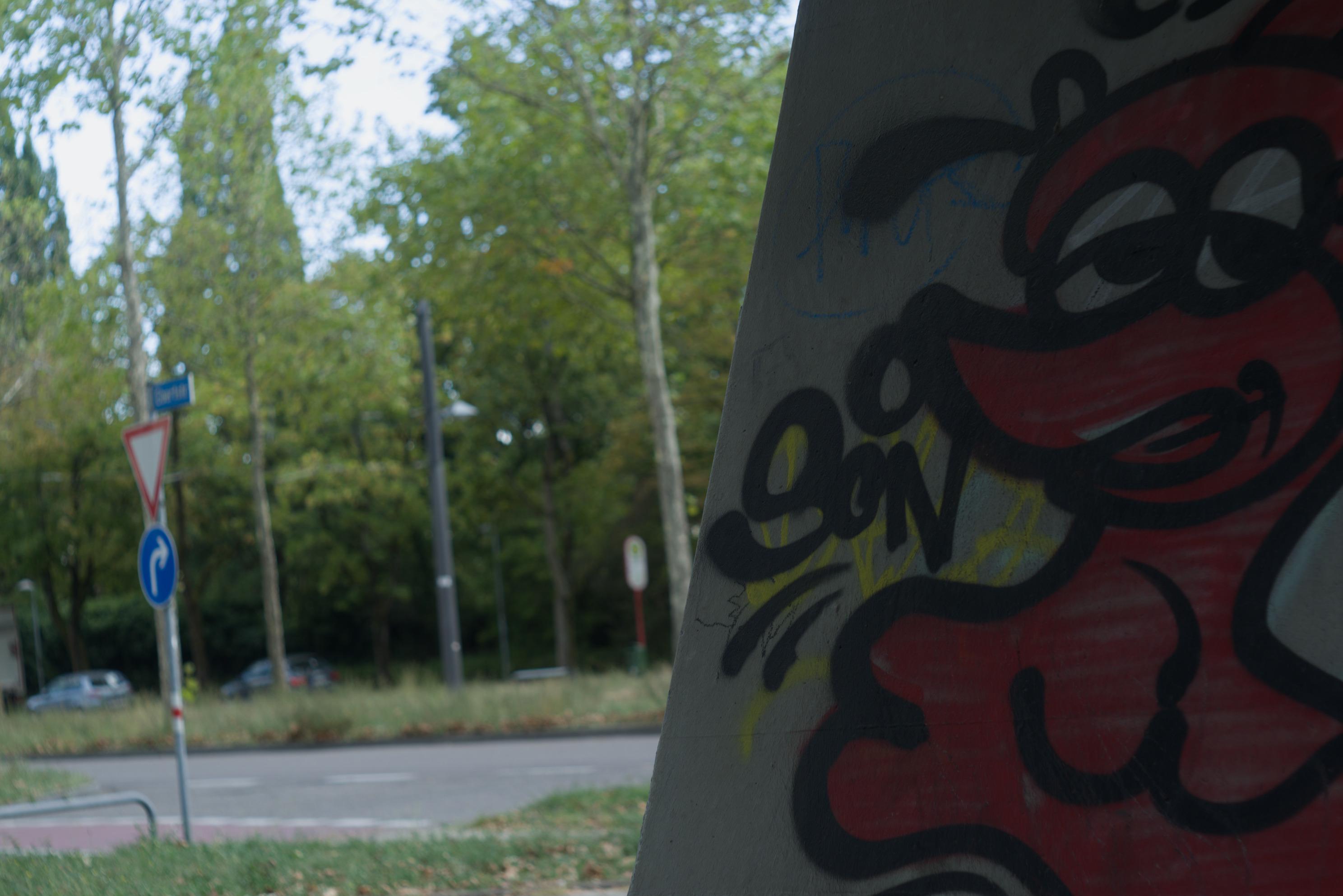 Silly graffiti guy framed next to the dull road of the prison which is Germany